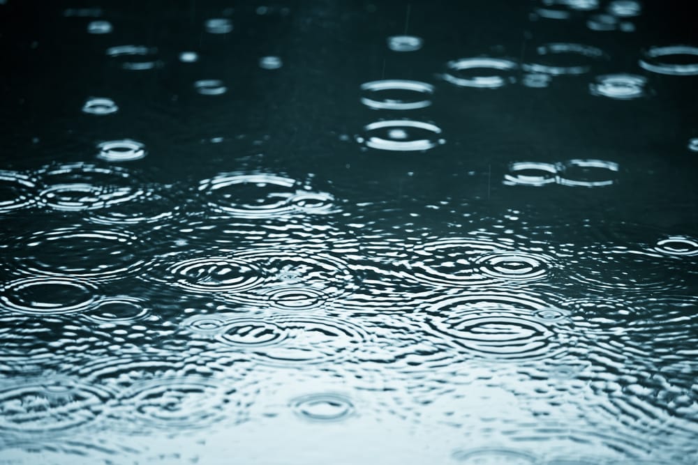 Rain drops rippling in a puddle with blue sky reflection